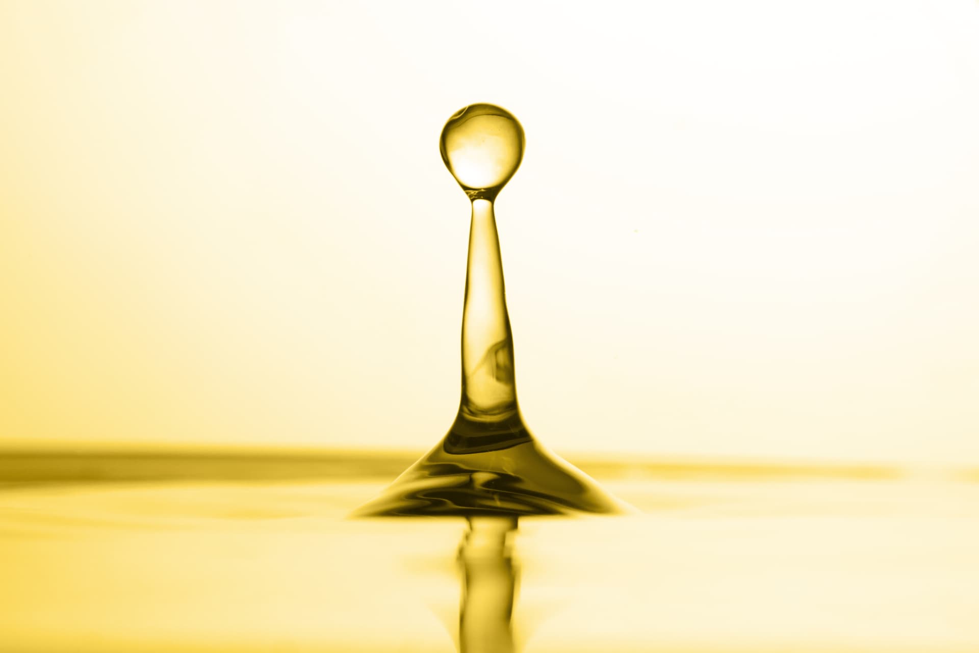 Golden edible oil droplet forming a crown on a reflective surface